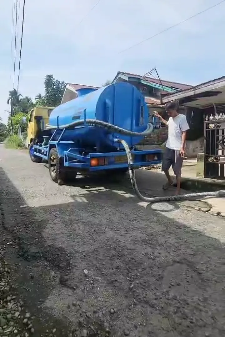 Truk tangki biru menyedot dengan selang di jalan permukiman